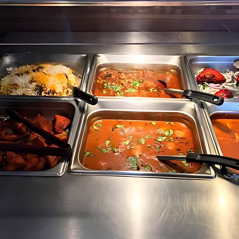 A buffet line at Biryani Bowl with various Indian dishes, including rice, curries, and tandoori chicken.