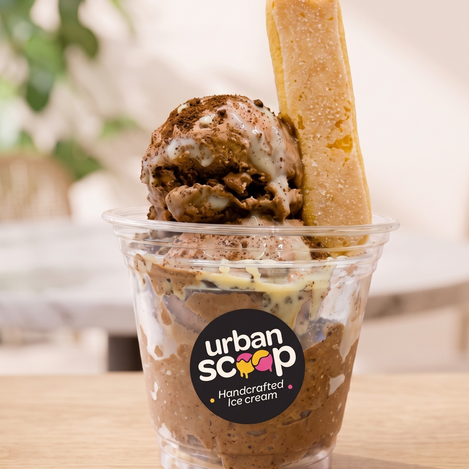 Urban Scoop handcrafted chocolate ice cream sundae in a clear cup, topped with whipped cream, chocolate crumbs, and a wafer biscuit.