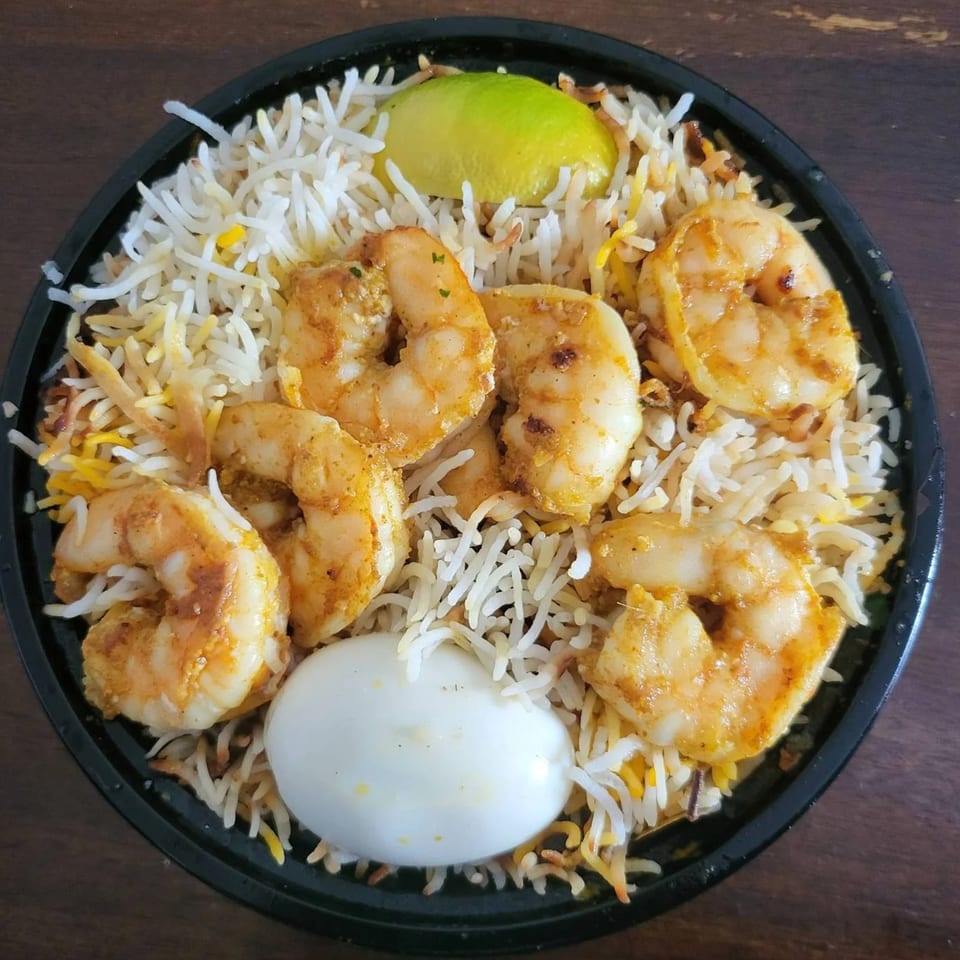Shrimp biryani with basmati rice, a hard-boiled egg, and a lime wedge in a black bowl.