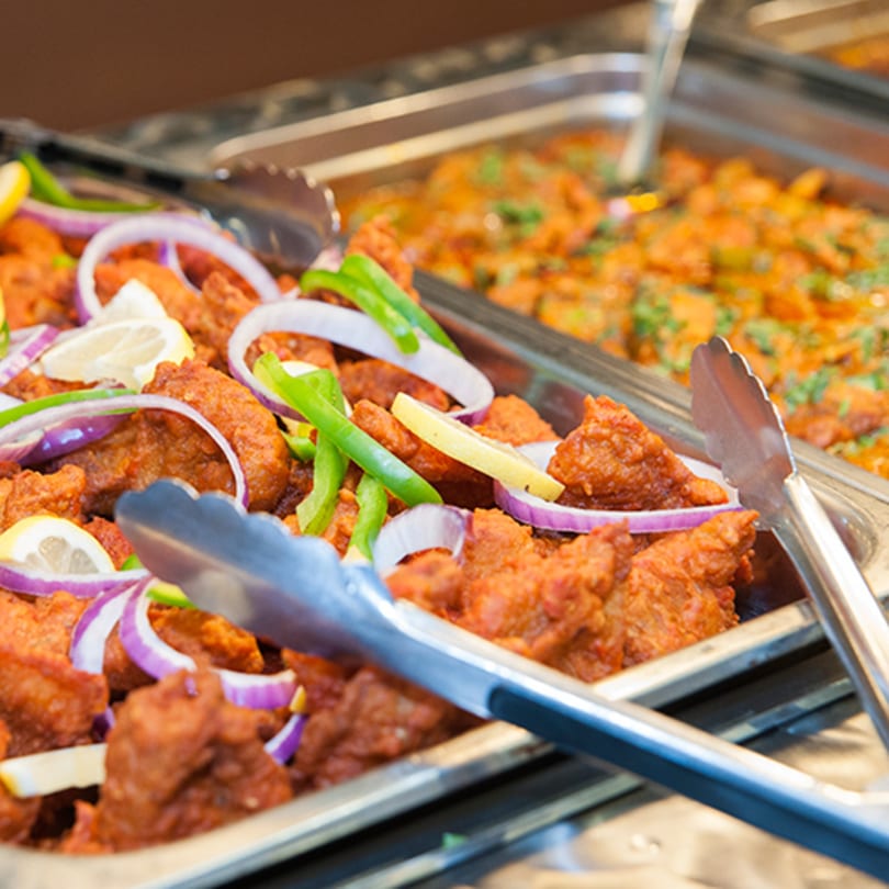 Indian buffet with chicken pakora, lemon, onions, and green peppers, alongside another curry dish.