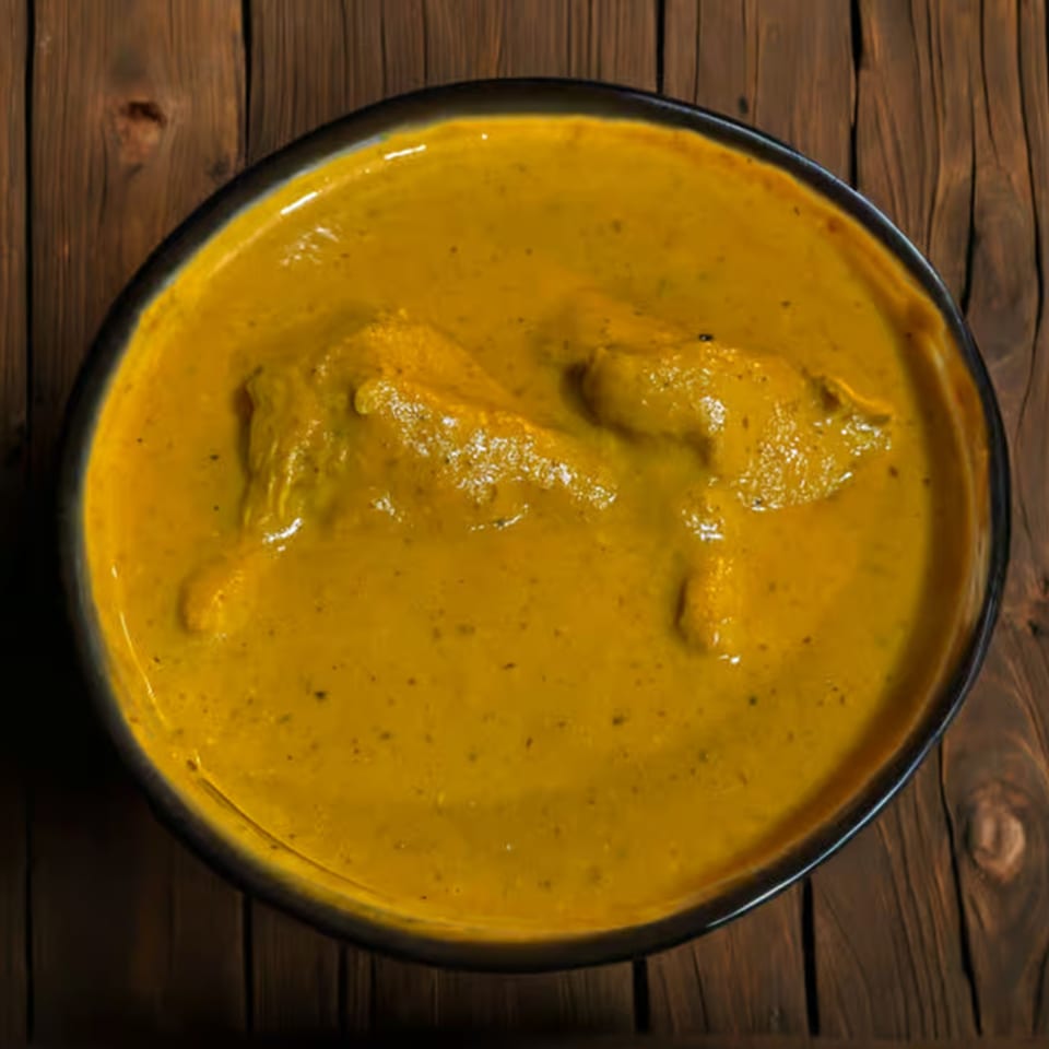 Overhead view of a bowl of creamy yellow Indian chicken curry on a rustic wooden table.